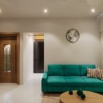 12x15 living room layout with a teal three-seater sofa, round wooden coffee table, large window with floor-to-ceiling curtains, minimalist false ceiling, and modern hall interior design.